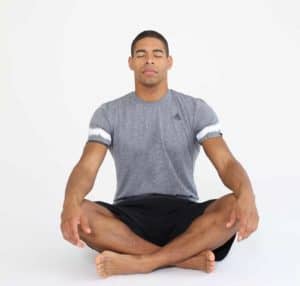 Mann sitzt im Schneidersitz mit geschlossenen Augen und entspannt sich