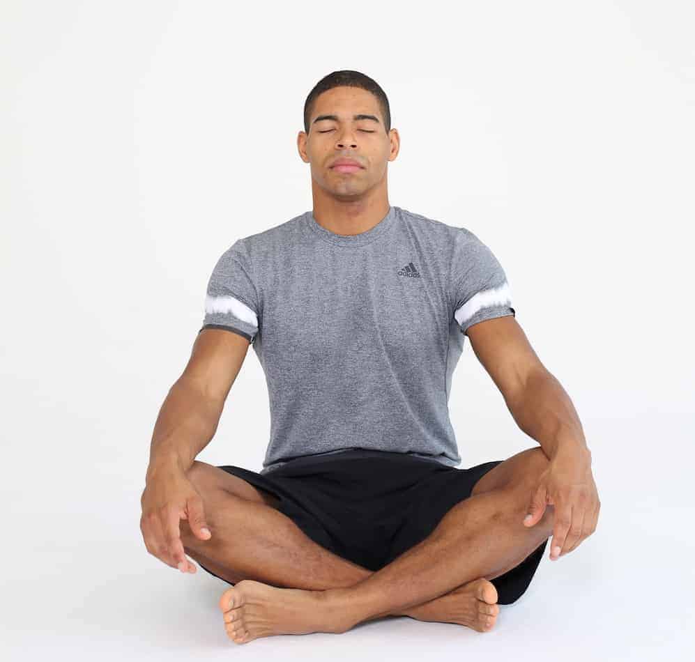 Mann sitzt im Schneidersitz mit geschlossenen Augen und entspannt sich