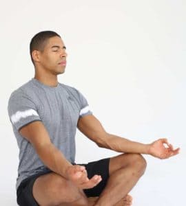 Mann sitzt im Schneidersitz und macht progressive Muskelrelaxation