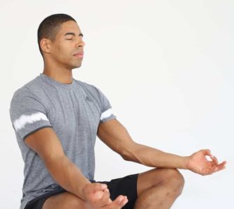 Mann sitzt im Schneidersitz und macht progressive Muskelrelaxation