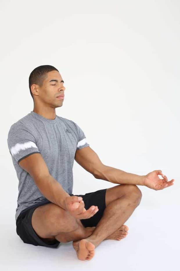 Mann sitzt im Schneidersitz und macht progressive Muskelrelaxation