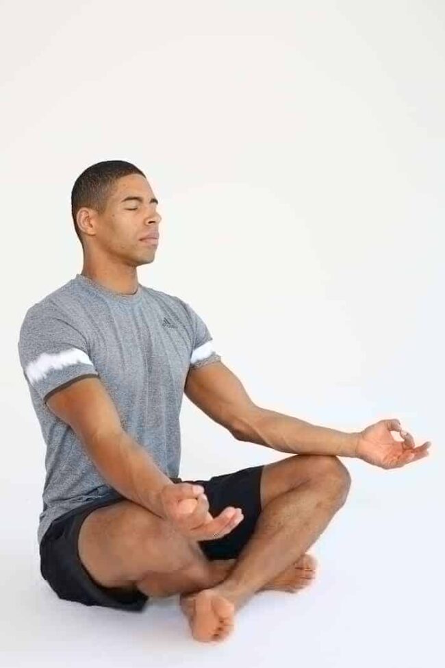 Progressive Muskelrelaxation Mann sitzt im Schneidersitz und macht progressive Muskelrelaxation