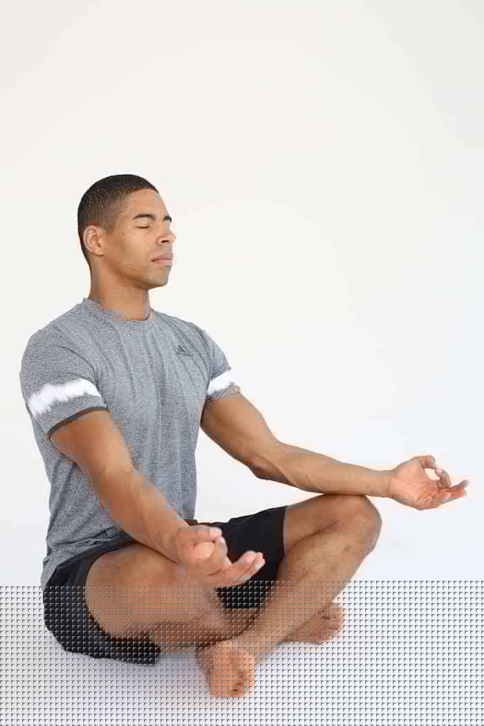 Mann sitzt im Schneidersitz und macht progressive Muskelrelaxation