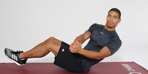 Mann macht Russian Twists auf dunkelroter Trainingsmatte