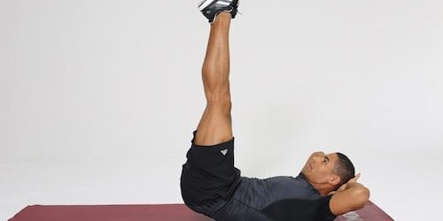 Mann macht Reverse Crunches auf dunkelroter Trainingsmatte