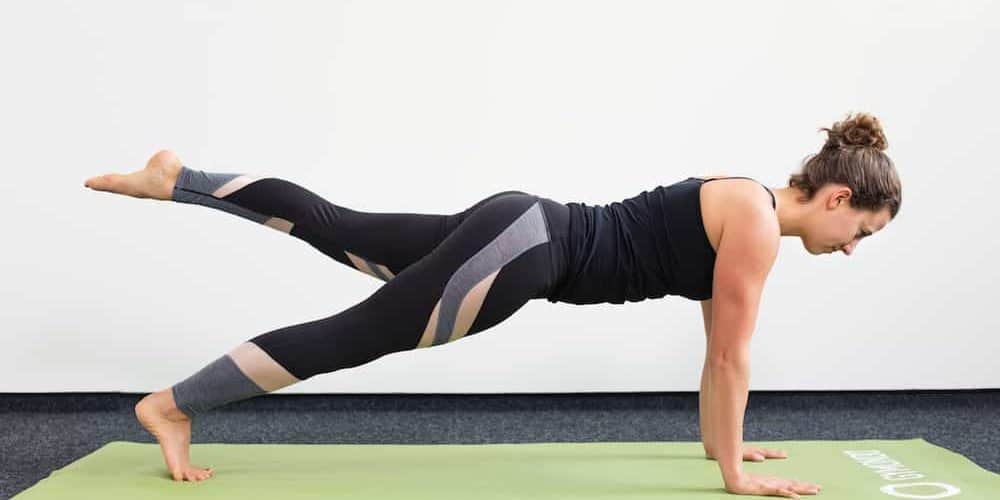 Leg Pull Front Junge Frau in Liegestützposition auf einer hellgrünen Trainingsmatte macht Pilates Leg Pull Front