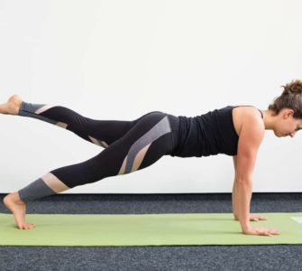 Junge Frau in Liegestützposition auf einer hellgrünen Trainingsmatte macht Pilates Leg Pull Front