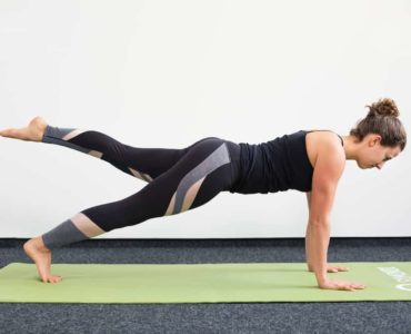 Junge Frau in Liegestützposition auf einer hellgrünen Trainingsmatte macht Pilates Leg Pull Front
