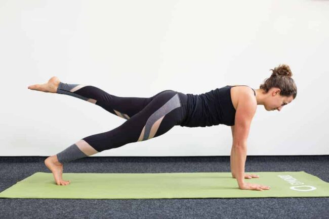 Leg Pull Front Junge Frau in Liegestützposition auf einer hellgrünen Trainingsmatte macht Pilates Leg Pull Front