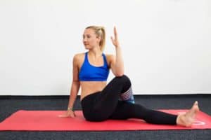 Junge Frau auf roter Trainingsmatte macht Yoga den sitzenden Twist