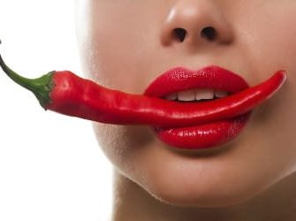 Frau mit Chilischote im Mund mit Lippenstift