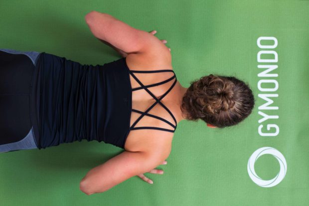 Junge Frau auf einer hellgrünen Trainingsmatte macht Liegestützen