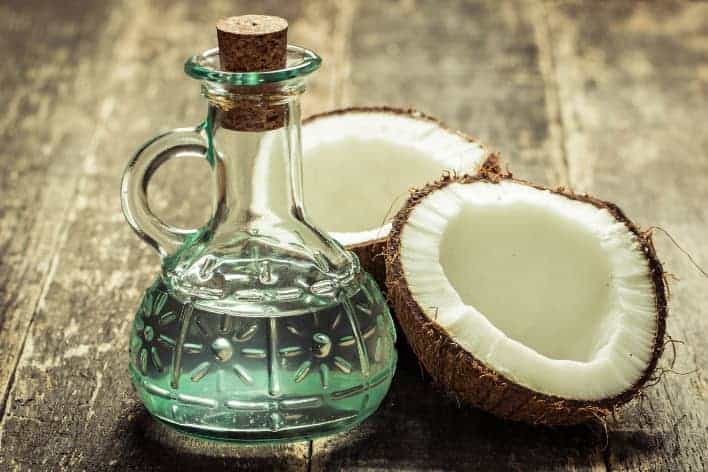kokosnussoel in Glaskaraffe mit aufgeschlagener Kokosnuss auf Holztisch