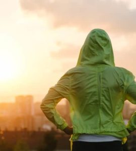 Frau mit grünem Kapuzenpulli schaut in den Sonnenuntergang.