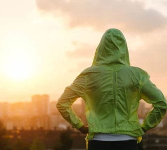 Frau mit grünem Kapuzenpulli schaut in den Sonnenuntergang.