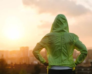 Frau mit grünem Kapuzenpulli schaut in den Sonnenuntergang.
