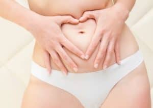 Frau fasst sich an ihre Problemzone Bauch und formt mit den Händen ein Herz.