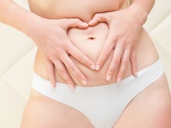 Frau fasst sich an ihre Problemzone Bauch und formt mit den Händen ein Herz.
