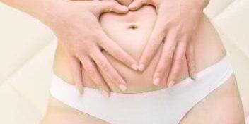 Frau fasst sich an ihre Problemzone Bauch und formt mit den Händen ein Herz.