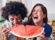 Zwei junge Frauen lachen und essen zusammen ein großes Stück Wassermelone