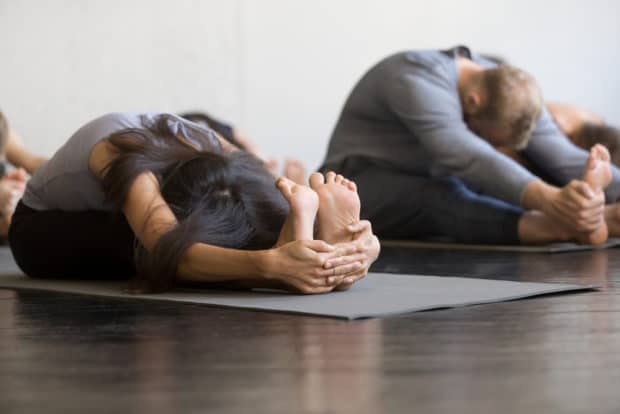 Eine Frau und ein Mann auf Yogamatten machen die sitzende Vorbeuge