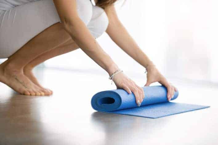 Frau rollt eine Fitness-Matte zusammen