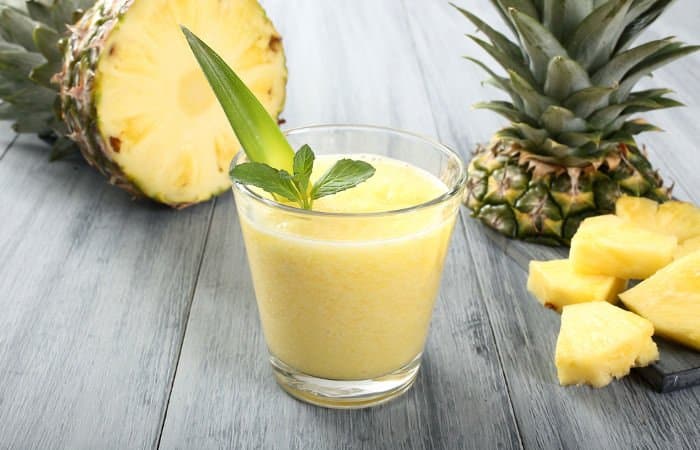 Ananassaft in einem Glas, dahinter eine aufgeschnittene Ananas