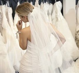Frau in Brautkleid vor einer Kleiderstange mit vielen weiteren Brautkleidern