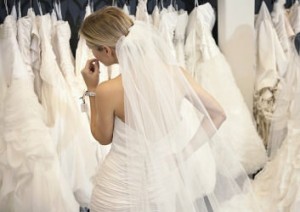 Frau in Brautkleid vor einer Kleiderstange mit vielen weiteren Brautkleidern