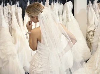 Frau in Brautkleid vor einer Kleiderstange mit vielen weiteren Brautkleidern