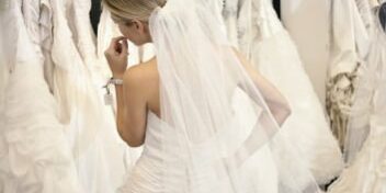 brautkleider_353 Frau in Brautkleid vor einer Kleiderstange mit vielen weiteren Brautkleidern