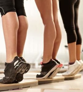 Drei Frauen, die auf einer Holzleiste Calf Raises ausführen