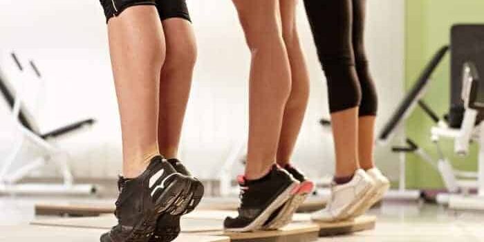 Drei Frauen, die auf einer Holzleiste Calf Raises ausführen