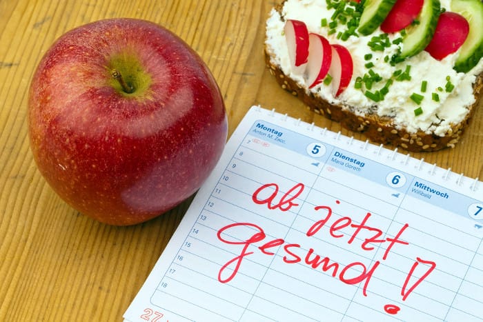 Apfel und mit Frischkäse bestrichenes Brot, daneben ein Zettel, auf dem 'ab jetzt gesund!' steht