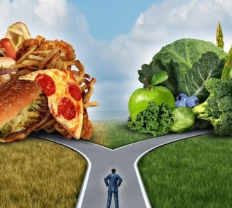 Mann im Anzug steht an einer Weggabelung zwischen Fastfood und grünem Gemüse