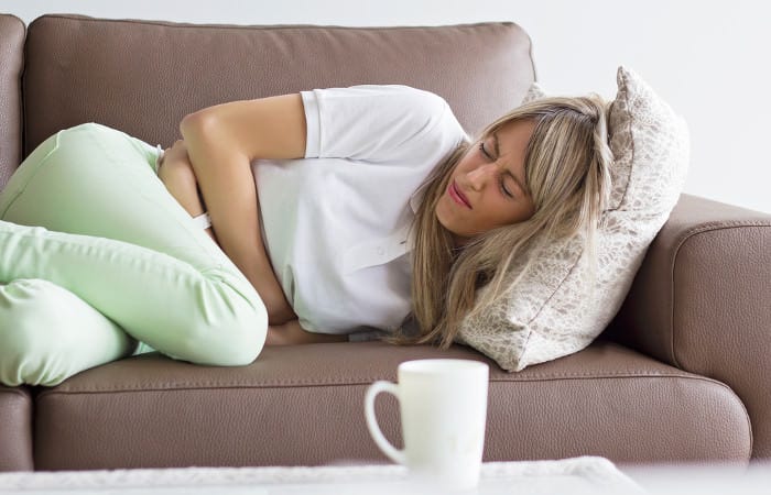 Frau krümmt sich mit Bauchschmerzen auf dem Sofa