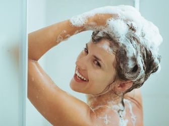 Duschende Frau beim Einshampoonieren ihrer Haare