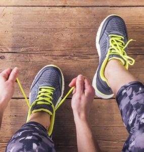 Sportlerin mit Muskelkater schnürt sich die Schuhe