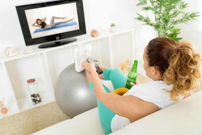 Sportlerin mit schlechten Vorsätzen vor dem Fernseher mit Bier