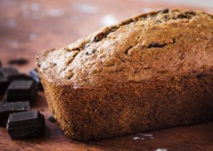 Ein Schokoladen-Zucchini-Kuchen mit danebenliegender Zucchini sowie Stücken dunkler Schokolade