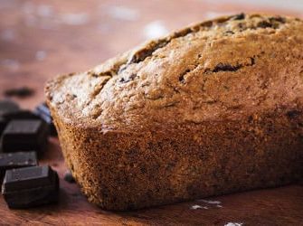 Ein Schokoladen-Zucchini-Kuchen mit danebenliegender Zucchini sowie Stücken dunkler Schokolade