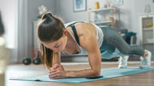Strong woman doing a plank on forearms in her cozy living room.