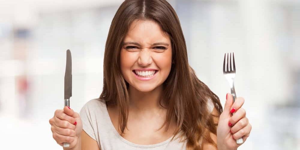 Hunger oder Heißhunger Frau mit Messer und Gabel in den Händen grinst