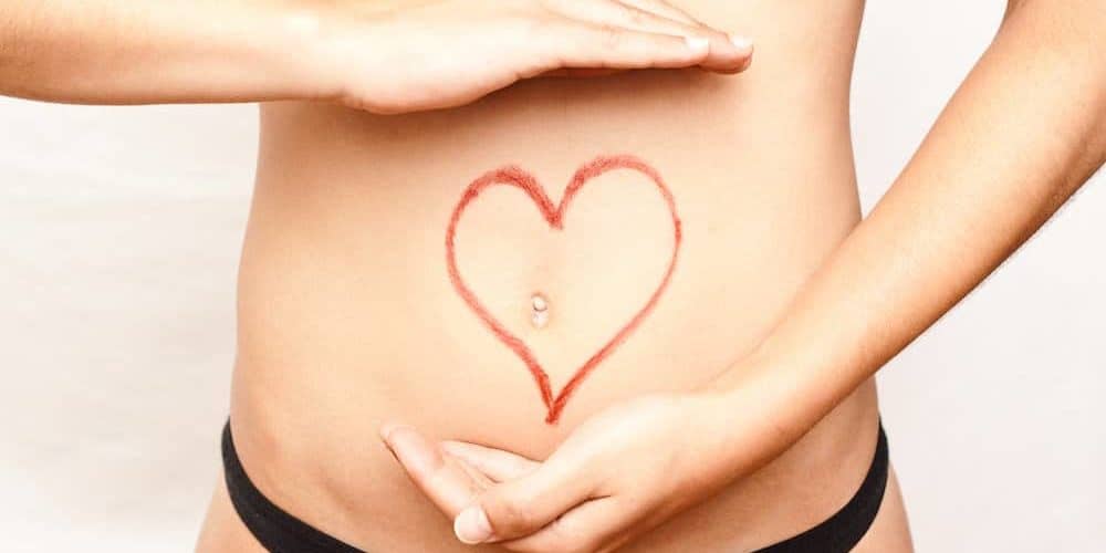 Bauch einer Frau mit rotem Stift wurde ein Herz um den Bauchnabel gezeichnet. Thema: Darm - Ursache für Übergewicht