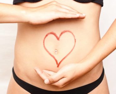 Bauch einer Frau mit rotem Stift wurde ein Herz um den Bauchnabel gezeichnet. Thema: Darm - Ursache für Übergewicht