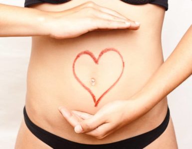 Bauch einer Frau mit rotem Stift wurde ein Herz um den Bauchnabel gezeichnet. Thema: Darm - Ursache für Übergewicht