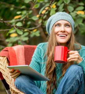 Junge Frau mit Mütze sitzt draußen in der Natur mit einer Tasse Mate Tee