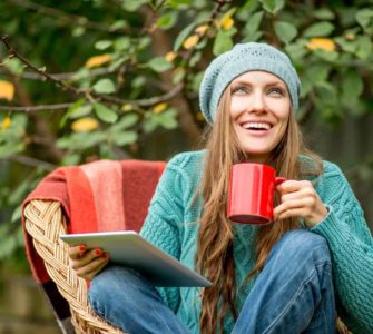 Junge Frau mit Mütze sitzt draußen in der Natur mit einer Tasse Mate Tee