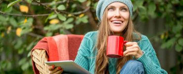 Junge Frau mit Mütze sitzt draußen in der Natur mit einer Tasse Mate Tee