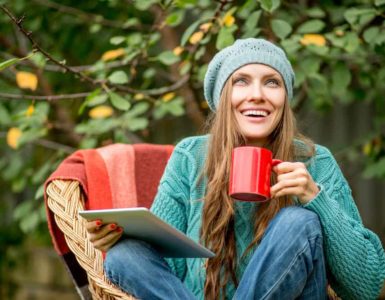 Junge Frau mit Mütze sitzt draußen in der Natur mit einer Tasse Mate Tee